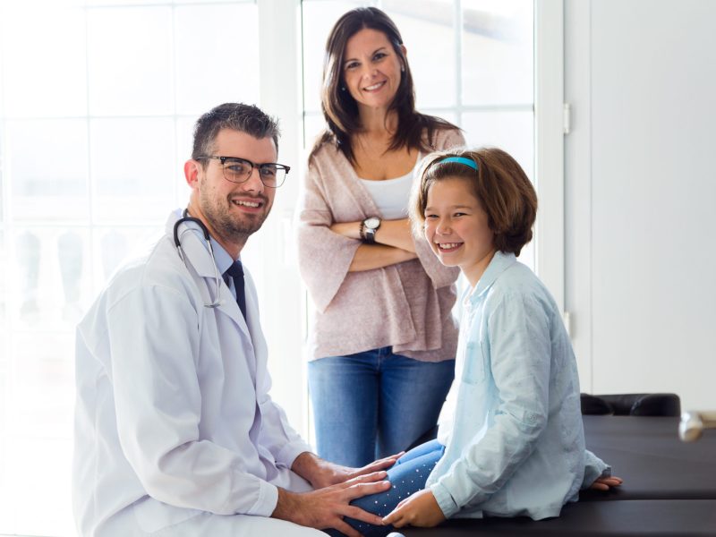 Portrait of mother and daughter with male doctor looking at camera in the office.