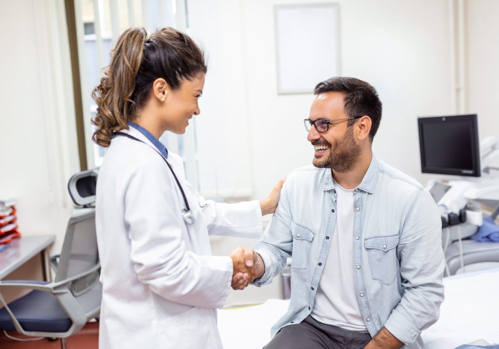 Smiling young female doctor shake hand close health insurance deal with elderly patient at consultation in hospital. Happy woman GP handshake greeting get acquainted with man in clinic.